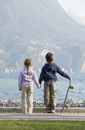 two children, brother and sister holding hands looking at the lakeの写真素材