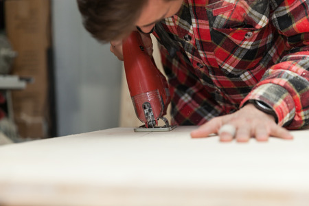 Young carpenter in his workshop using an electric saw to cut a wooden plank の写真素材