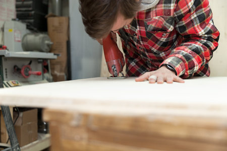 Young carpenter in his workshop using an electric saw to cut a wooden plank 