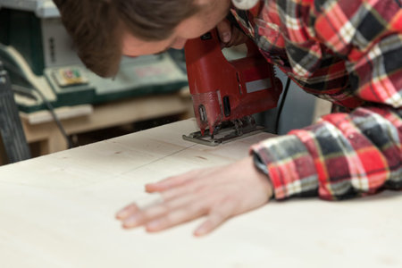 Young carpenter in his workshop using an electric saw to cut a wooden plank 