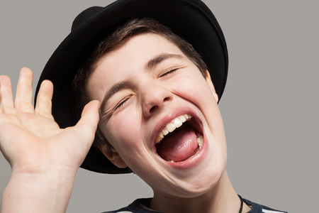 Boy with hat laughs amused, portrait in studioの写真素材