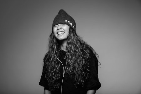 Young woman with hat and headset in ears laughs. Portrait studio