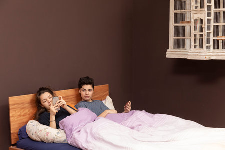 A young girl and a young boy together in the double bed. Even if they are together everyone is alone...