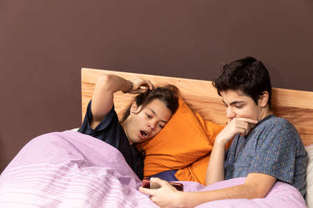 Couple in bed watching a movie or news together on a phone.の写真素材