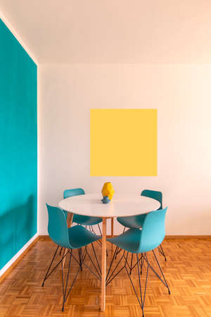 Detail of modern table and chairs with parquet floor, yellow frame and turquoise wall. Front view. Nobody insideの写真素材