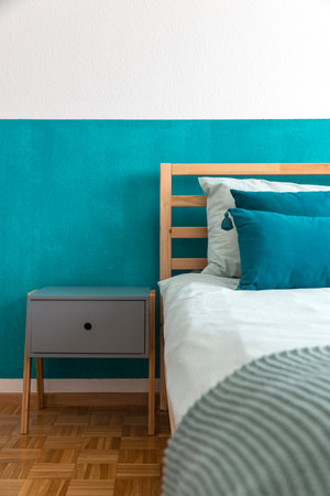 Detail of wooden bed with turquoise wall and many pillows on the sheets. Feeling of intimacy and...