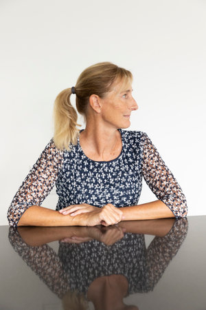 Middle aged woman portrait in profile with blonde hair tied in a ponytail with a white wall behind. Reflective table and white backgroundの写真素材