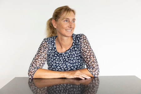 Middle aged woman portrait in profile with blonde hair tied in a ponytail with a white wall behind. Reflective table and white backgroundの写真素材