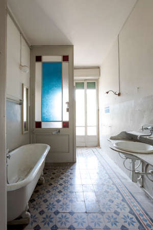 Old bathroom with outside bathtub, exposed pipes, and black and white tiles. Interior of an abandoned villa to be restored.の写真素材