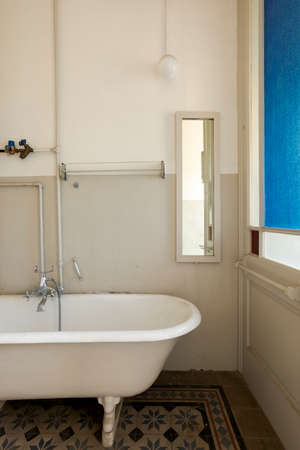 Old bathroom with outside bathtub, exposed pipes, and black and white tiles. Interior of an abandoned villa to be restored.の写真素材