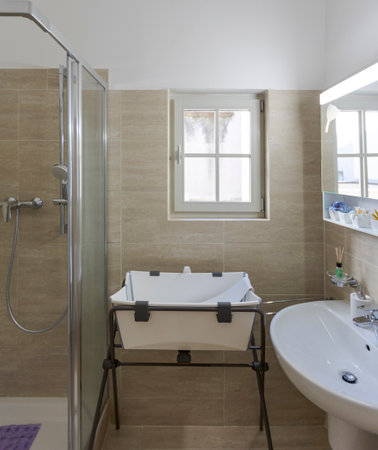 Front view of a bright bathroom with a window, a bathtub for babies, a sink with a mirror above it. Nobody insideの写真素材