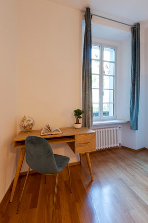 Detail of a wooden desk and an elegant blue chair and a bright window on the right. Ideal location for smartworking. Nobody insideの写真素材