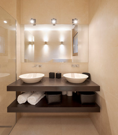 Modern bathroom front view with large light marble slabs. There are two sinks with a large mirror illuminated by spotlights. Nobody insideの写真素材