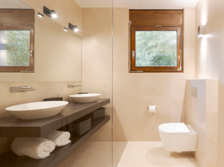 Modern bathroom front view with large light marble slabs. There are two sinks with a large mirror illuminated by spotlights. Nobody insideの写真素材