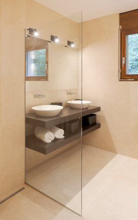 Modern bathroom with large light marble slabs. There are two sinks with a large mirror illuminated by spotlights. Nobody insideの写真素材