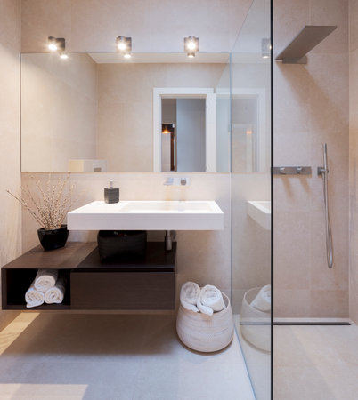 Modern bathroom front view with large light marble slabs. There are two sinks with a large mirror illuminated by spotlights. Nobody insideの写真素材
