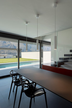 Dining room detail with modern chairs and a red sofa. Outside the window is the pool and green lawn. Nobody insideの写真素材