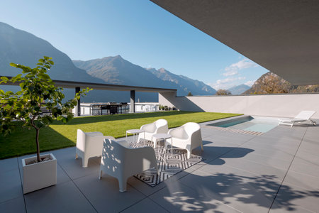 Modern house with garden. In the foreground is a small living room with armchairs and small tables; at the back is the pool with a deck chair. Nobody insideの写真素材