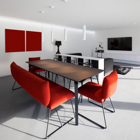 Modern living room with red bench and armchair with table lit by hanging lamps. there is a low bookcase and a large wall-mounted TV. Nobody insideの写真素材