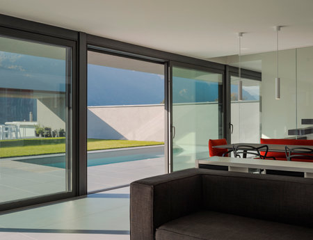 Interior modern villa living room with large windows. Outside there is a swimming pool. Sunny day in the Alps of Switzerland. Nobody insideの写真素材