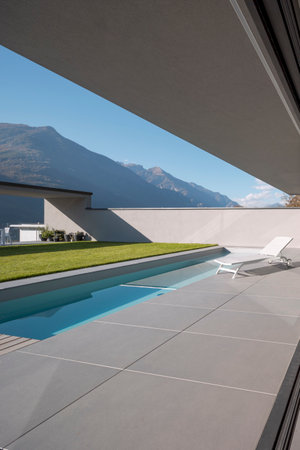 Garden of modern villa with swimming pool and a deck chair for relaxing. Sunny day in the Alps of Switzerland. Nobody insideの写真素材