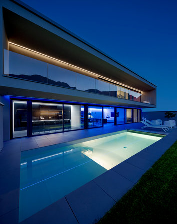 Modern house with swimming pool and garden in night scene illuminated by colored LED lights. Behind the house is the hill with the forest. Nobody insideの写真素材