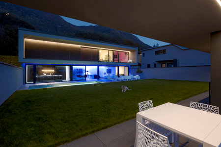 Modern house with swimming pool and garden in night scene illuminated by colored LED lights. Behind the house is the hill with the forest. Nobody insideの写真素材