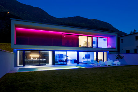Modern house with swimming pool and garden in night scene illuminated by colored LED lights. Behind the house is the hill with the forest. Nobody insideの写真素材