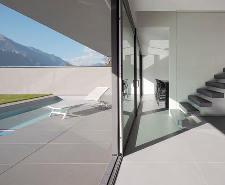 Interior modern villa with cantilevered staircase and large finistre. Outside is a swimming pool with a deck chair for relaxing. Sunny day in the Alps of Switzerland. Nobody insideの写真素材