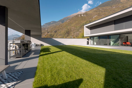 Manicured garden of modern villa surrounded by mountains. Sunny day. Nobody insideの写真素材