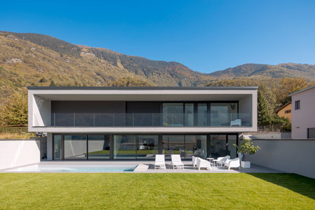 Front view modern house with two floors, pool two deck chairs and a small lounge with white armchairs. In front is a beautiful green lawn. Nobody insideの写真素材