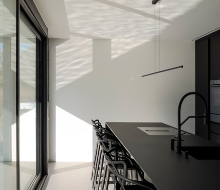 Black modern kitchen with sink and stools. There are bright windows where lots of light comes in. Nobody insideの写真素材
