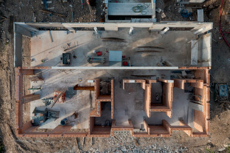 Aerial drone view of an outbuilding under construction, roofless with walls made of bricks. Around it is the building site. Nobody insideの写真素材