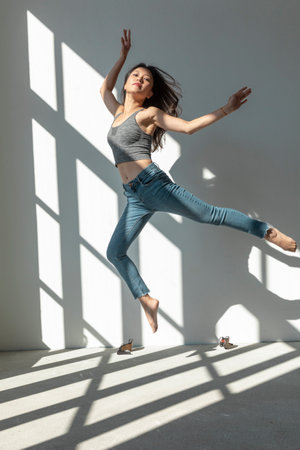 Asian dancer girl makes an acrobatic jump illuminated by the sun that enters through the window in an empty building. isolatedの写真素材