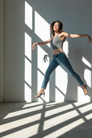 Asian dancer girl makes an acrobatic jump illuminated by the sun that enters through the window in an empty building. isolatedの写真素材
