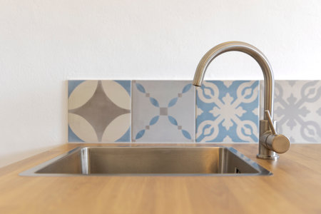 In the foreground there is a sink made of stainless steel with a top made of wood. Behind it are blue tiles and a white wall. Modern kitchen detailの写真素材