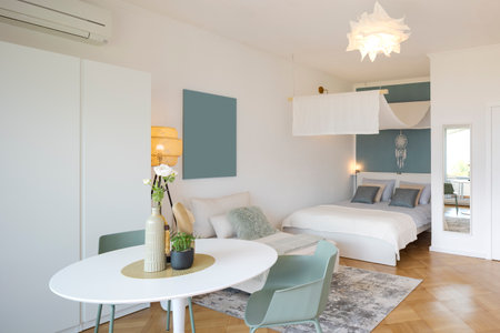 Interior of a studio apartment with a table with vases and flowers on it in the foreground. In the background is a bed with a modern canopy. Minimalist and elegant. No one inside.の写真素材