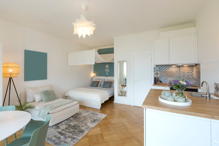 General view of a stylish modern studio apartment. There is a small kitchen with a wooden counter, a double bed and a single bed, and a table with chairs. No one insideの写真素材