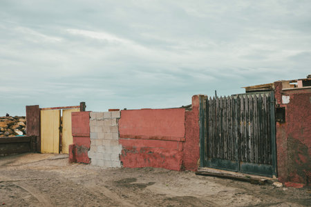 Orange wall with a green gate in a state of disrepair near the beach, the sky is cloudy on a spring day. No one insideの写真素材