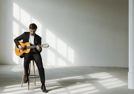 Portrait of a young boy playing the guitar. He is wearing a black suit. Interior of a renovated former factory.の写真素材