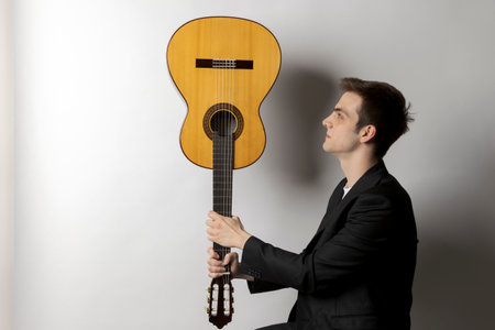 Young boy holds his guitar upside down and looks at it intently. White backgroundの写真素材