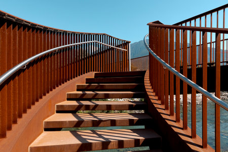 Detail of a stairway of a modern rusty bridge, with a clear blue sky behind it. Strong contrast between lights and shadows. Nobody insideの写真素材