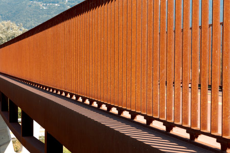 Detail of modern rusty orange colored pedestrian and bicycle bridge railing. Strong contrast of light and shadow, abstract. No one insideの写真素材