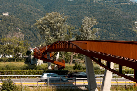 Modern rusted pedestrian and bicycle bridge with flowing Ticino river below. Beautiful panorama, immersed in the Alps of Italian Switzerland, nobody insideの写真素材