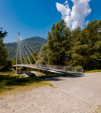 Modern pedestrian bridge in the middle of the mountains of Italian Switzerland, allowing you to cross the Ticino River. Sunny summer day.の写真素材
