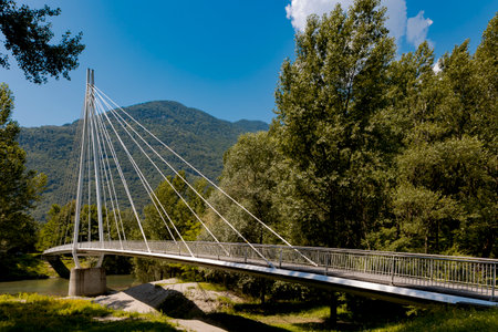 Modern pedestrian bridge in the middle of the mountains of Italian Switzerland, allowing you to cross the Ticino River. Sunny summer day.の写真素材
