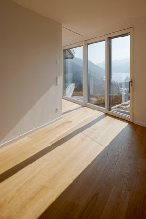 Interior of a modern apartment with wooden floors. Sunlight streams through the window providing a picturesque view of Switzerland's mountains and lake. No one present.の写真素材