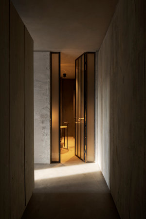 Dark hallway with rough concrete walls. At the end is an open glass door that gives a glimpse of the modern bathroom. No one insideの写真素材