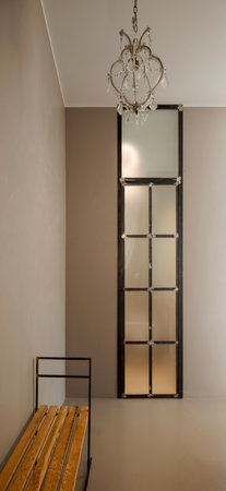 Front view of a hall with a little wooden bench and a big, bright window. No one is inside.の写真素材