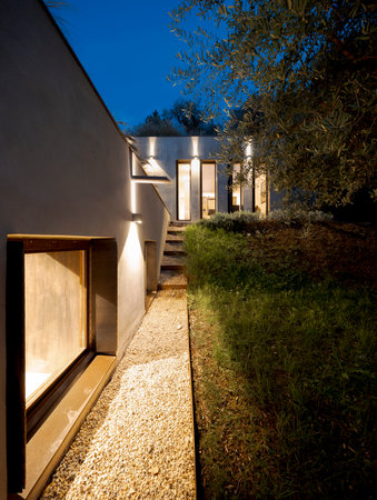 Contemporary house surrounded by olive trees, built on terraced land. Front view in night scene. No one is inside.の写真素材
